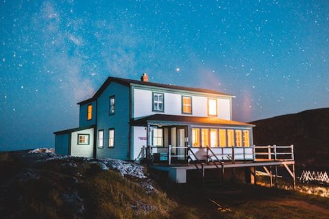 A house with a deck and a balcony is lit up at night.